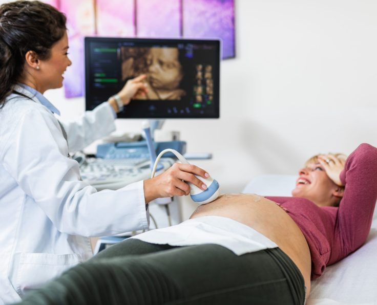 Beautiful and happy expectant mother at gynecological examination with ultrasound medical equipment.