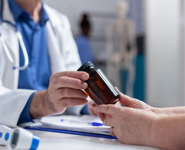 Close up of specialist giving bottle of pills to old woman at annual checkup visit. Hands of medic holding jar with prescription medicine and treatment to help cure illness. Medical remedy