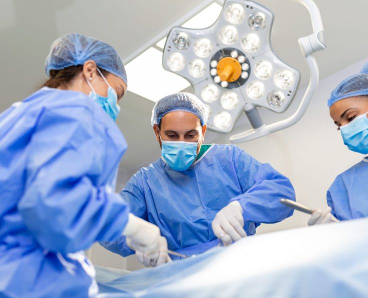 Surgeons doing surgery in operating theatre. Male and female surgeons operating patient. Medical professionals are wearing scrubs.